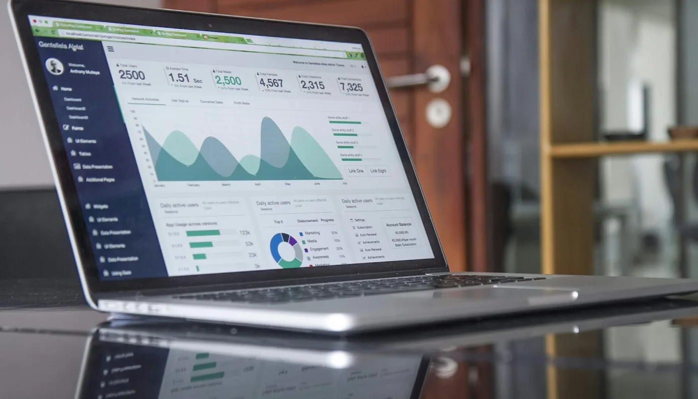 Laptop auf einem Glastisch zeigt ein Analytics-Dashboard mit Nutzerzahlen und Verlaufskurven